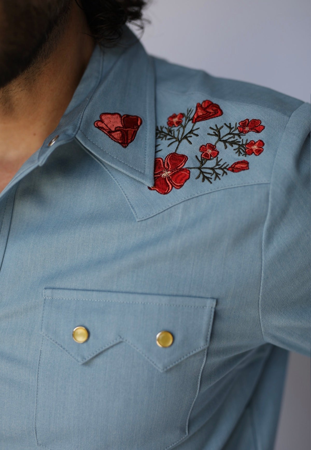 Close-up of red poppy embroidery and pearl snap sawtooth pocket on the HBarC x Gibson Dove chambray shirt.