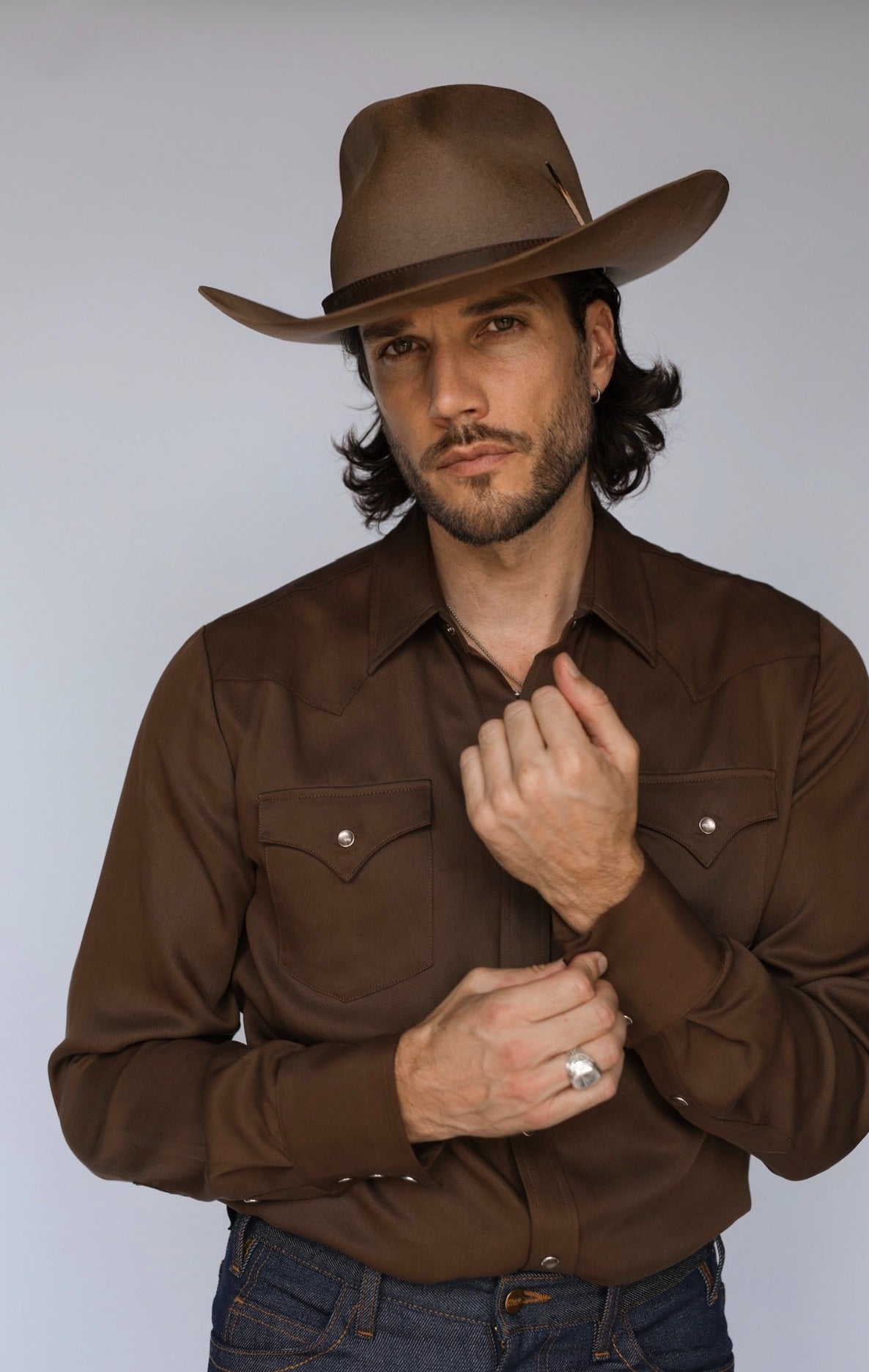 Man fastening the cuff of the H Bar C Denver chocolate western shirt, worn with a brown felt hat.