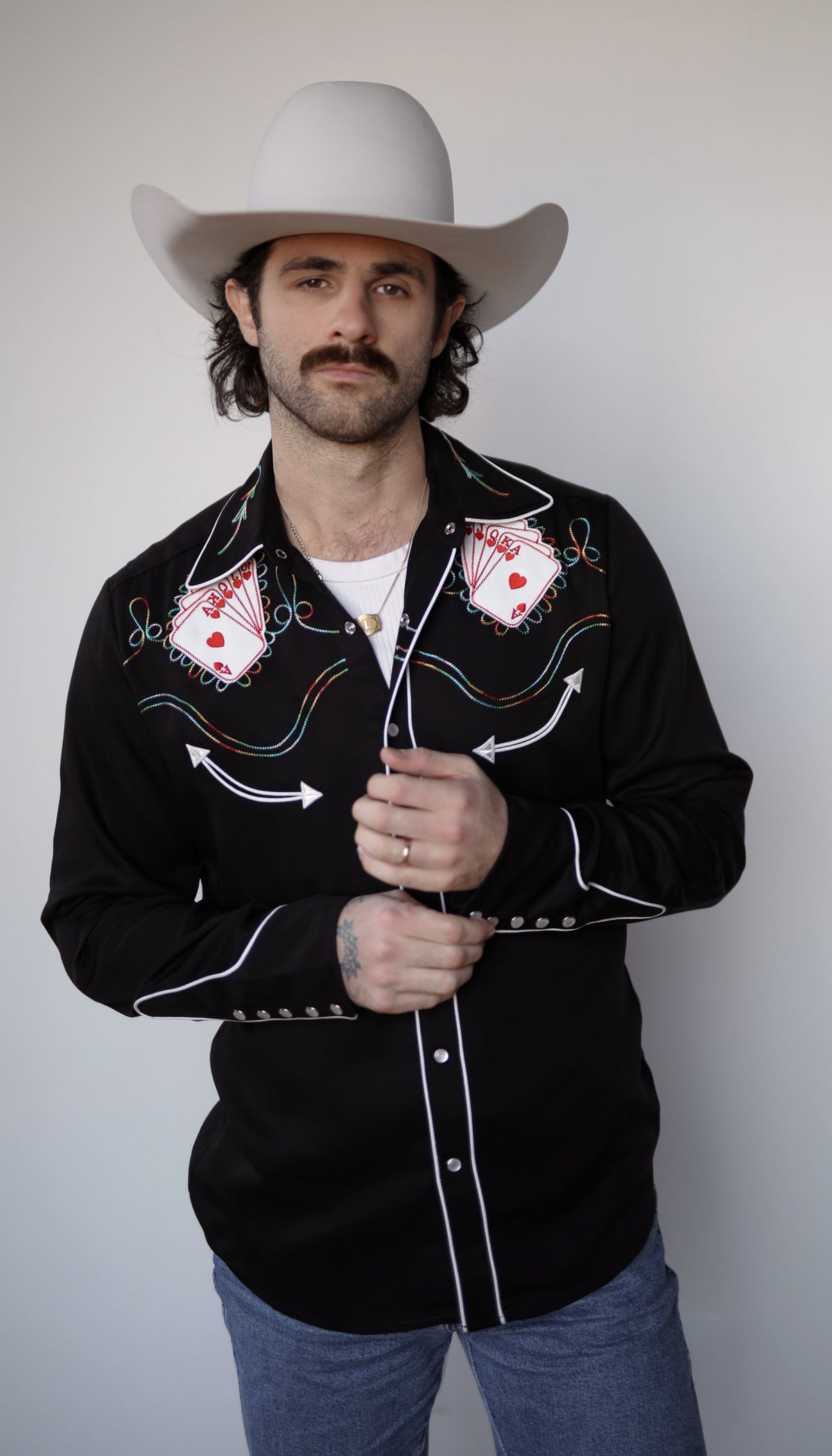 Man buttoning the H Bar C Royal Flush black shirt with playing card embroidery on the yokes.