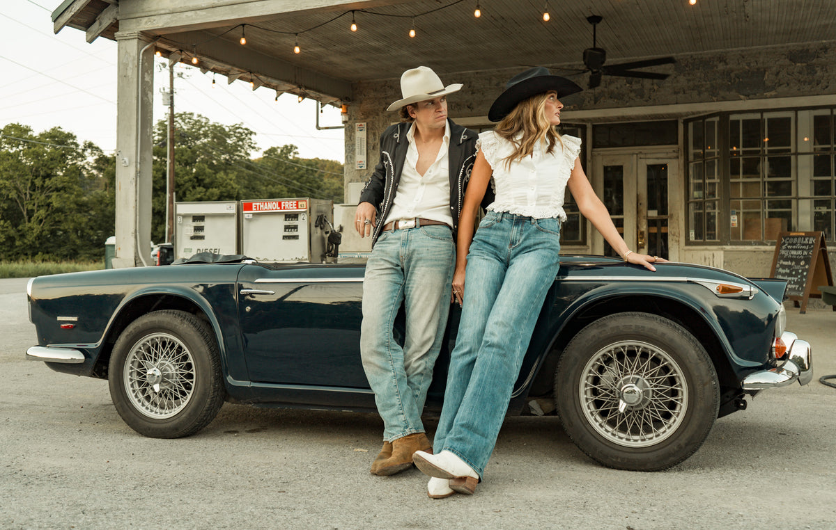 Two people standing next to a vintage car in front of a building.