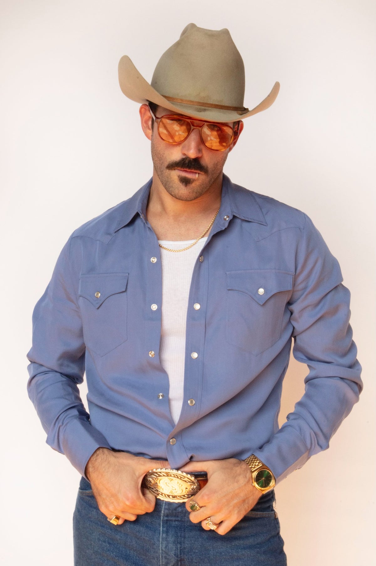 Man in a cowboy hat and tinted sunglasses wearing the H Bar C Denver men's shirt in periwinkle blue with a gold buckle.