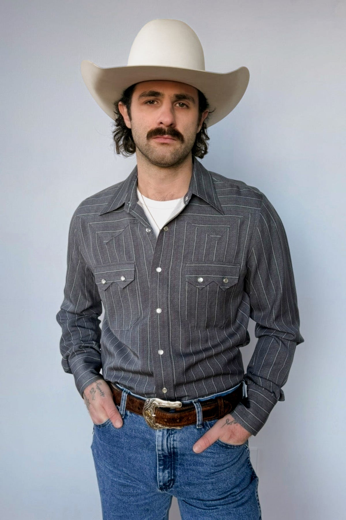 Man with hands in pockets wearing the H Bar C Tiger western shirt and cream hat.