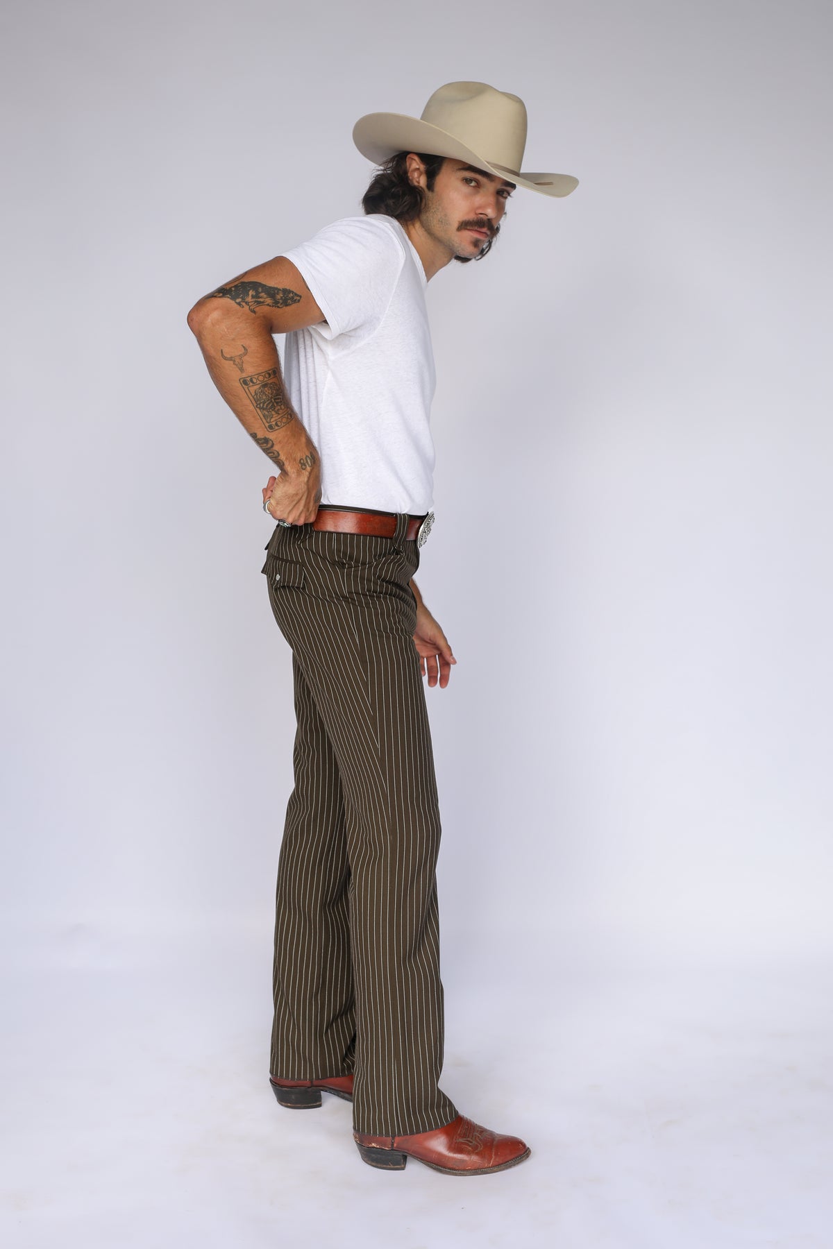Side pose in the H Bar C Bakersfield brown pinstripe western pants with cowboy hat and boots.