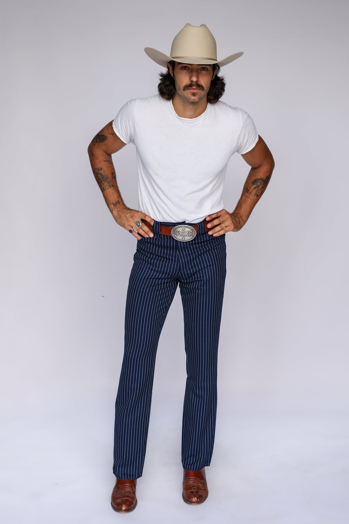 Man in a cream cowboy hat wearing the H Bar C Bakersfield western pants in navy pinstripe with a white tee and silver buckle.