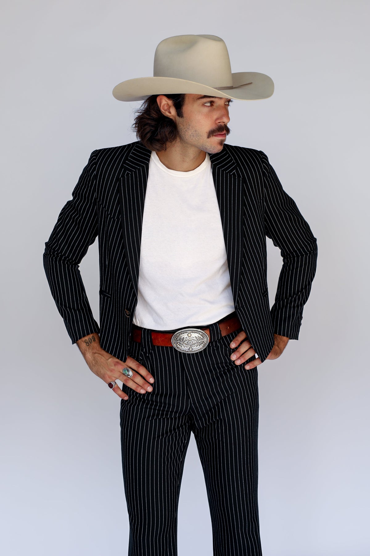 Front view of the H Bar C Bakersfield black pinstripe jacket open over a white tee with silver buckle.
