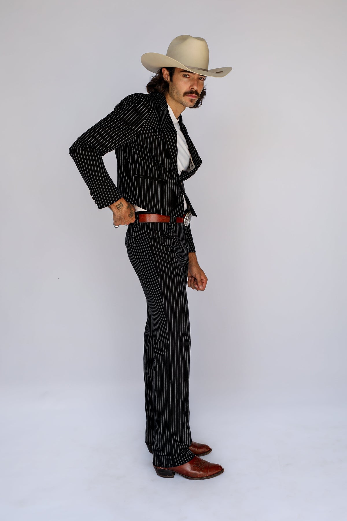 Side view of a man in a cowboy hat wearing the H Bar C Bakersfield black pinstripe western suit.