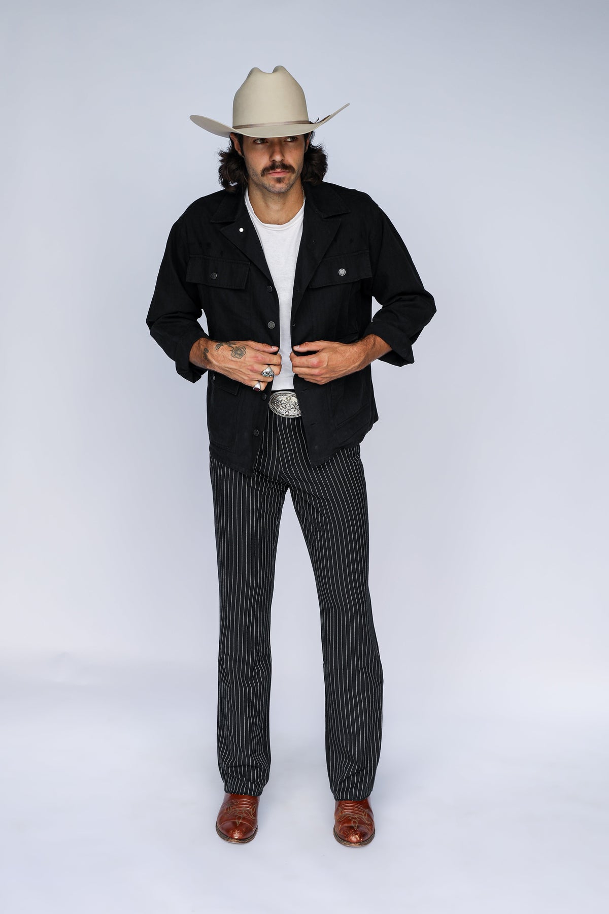 Full length view of the H Bar C Normandy black chore coat with pinstripe trousers and brown boots.