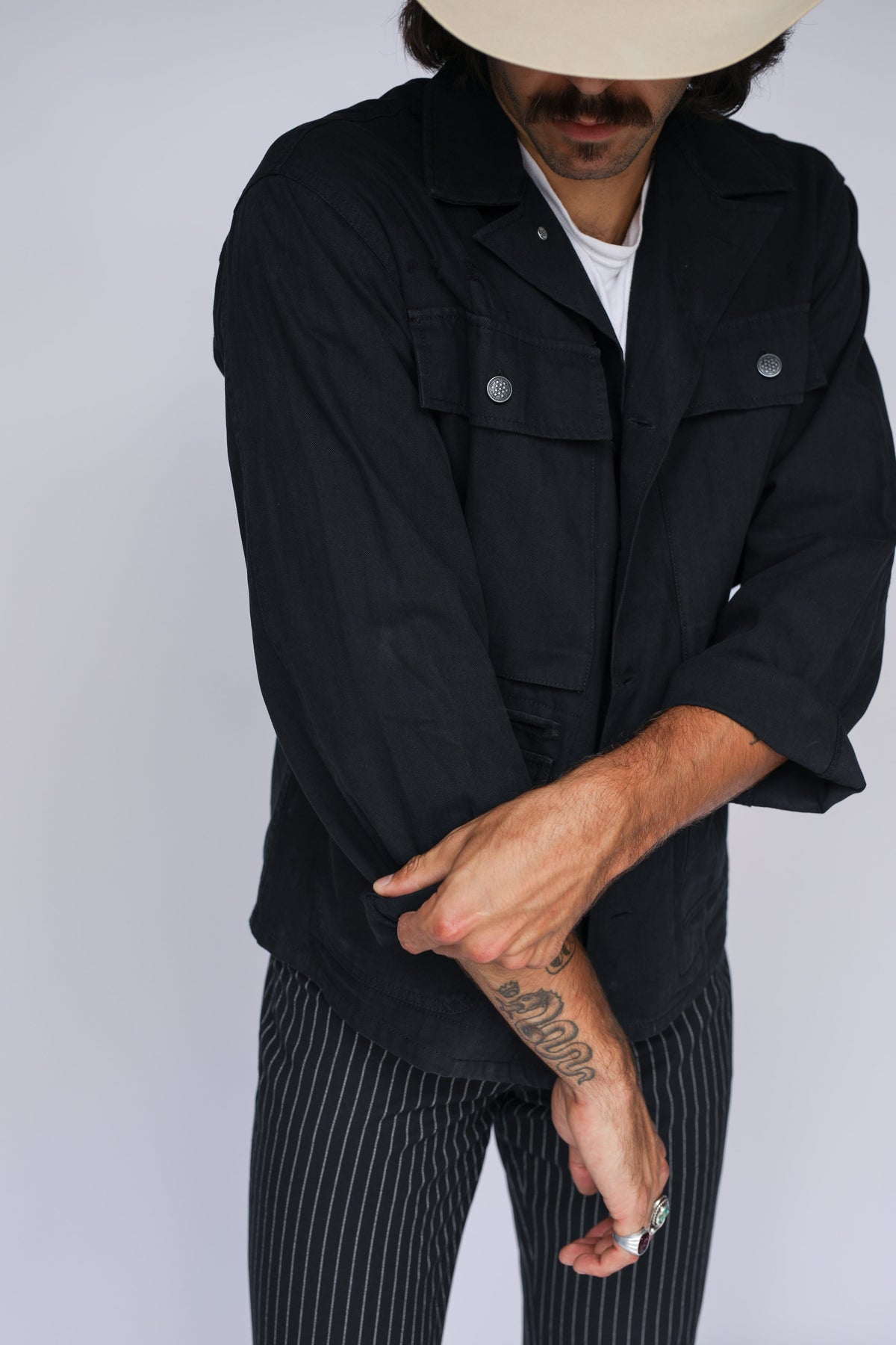 H Bar C Normandy black chore coat with a white tee and pinstripe trousers.