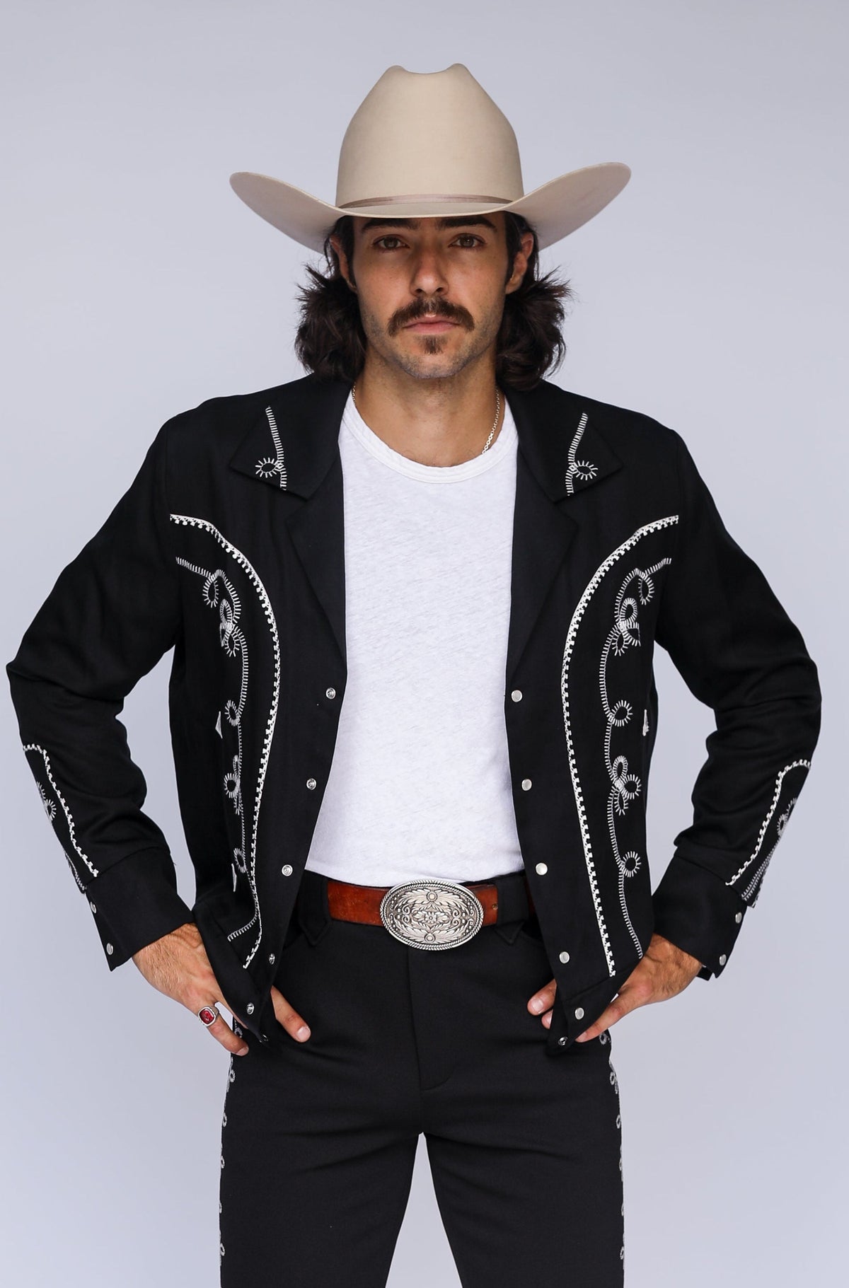 Man wearing the H Bar C Bolero men's jacket in black and white with chain stitch embroidery and horseshoe appliqué, cream cowboy hat, iconic 1936 western jacket.