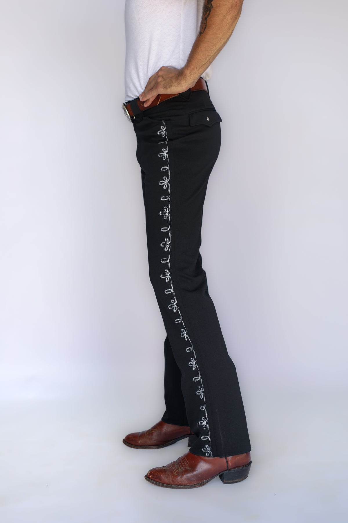 Side profile of the H Bar C Bolero black pants showing the white chain stitch embroidery from hip to hem.