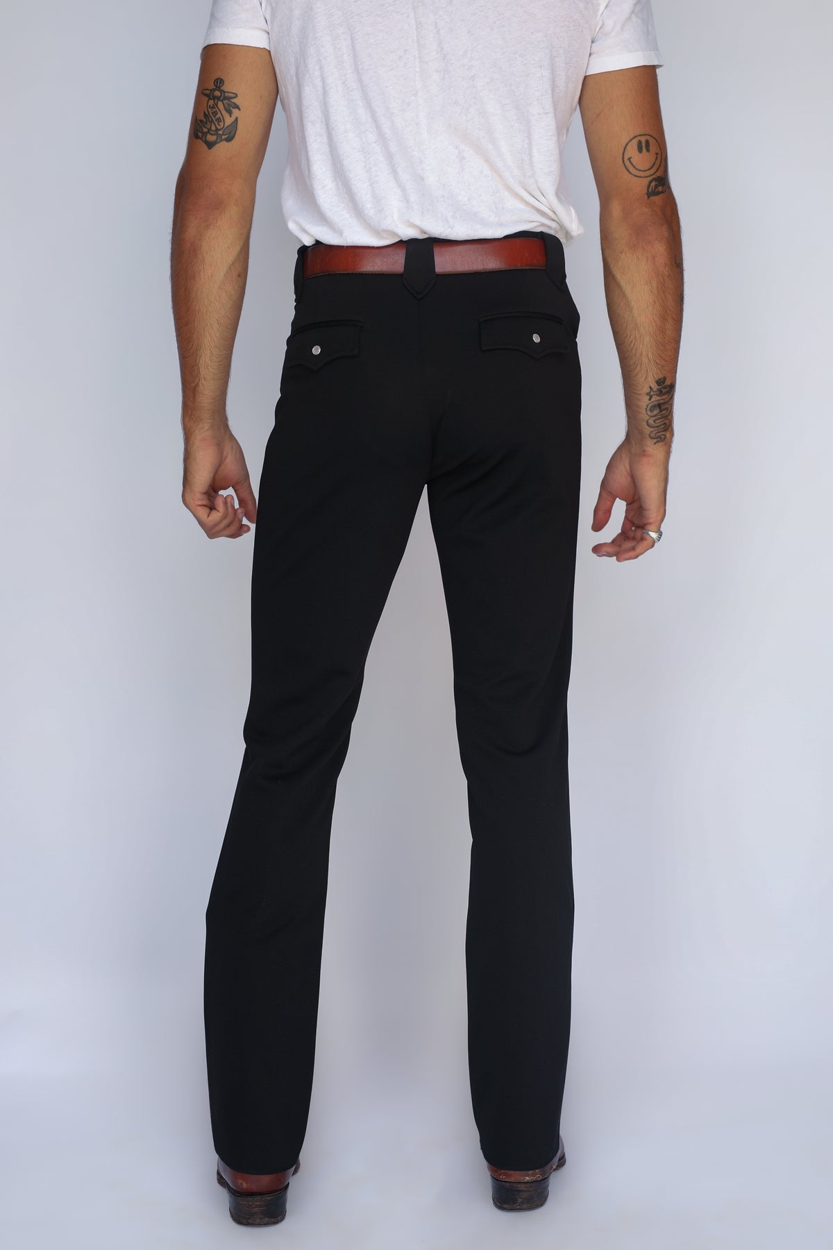 Back view of the H Bar C Bolero pants in black worn with a white tee, brown belt, and cowboy boots.