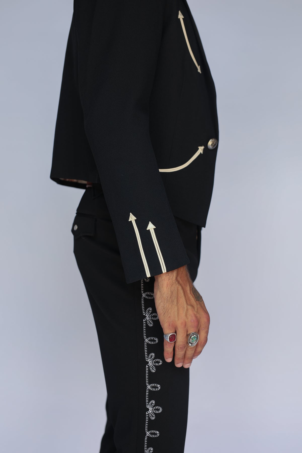 Side detail of the H Bar C Calamity men's black jacket sleeve with cream arrow trim, paired with embroidered western pants.
