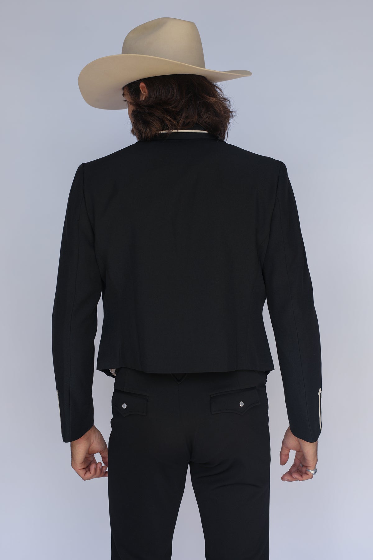 Back view of the H Bar C Calamity men's black cropped western blazer worn with a cream cowboy hat.