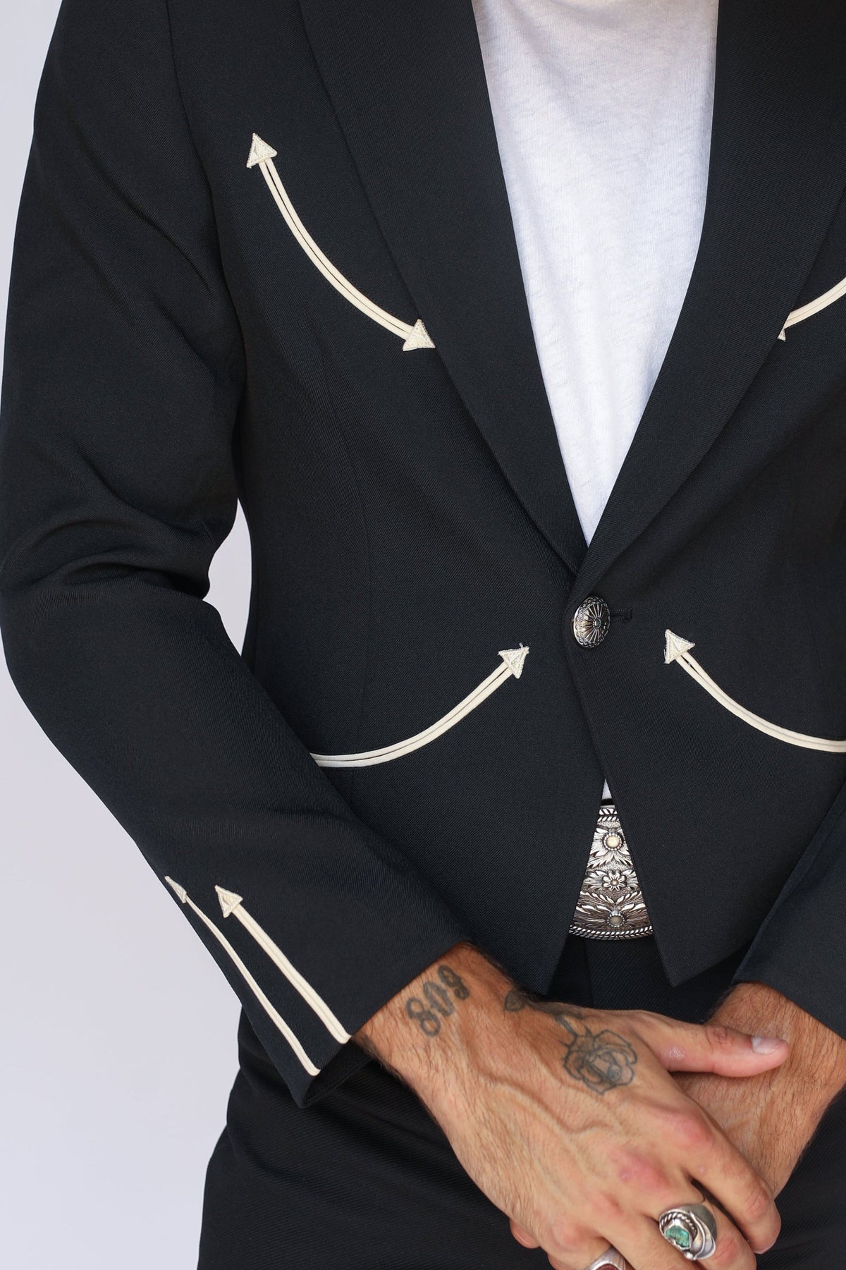 Close-up of the cream embroidered arrows on the lapel, smile pockets, and cuff of the H Bar C Calamity men's black jacket.