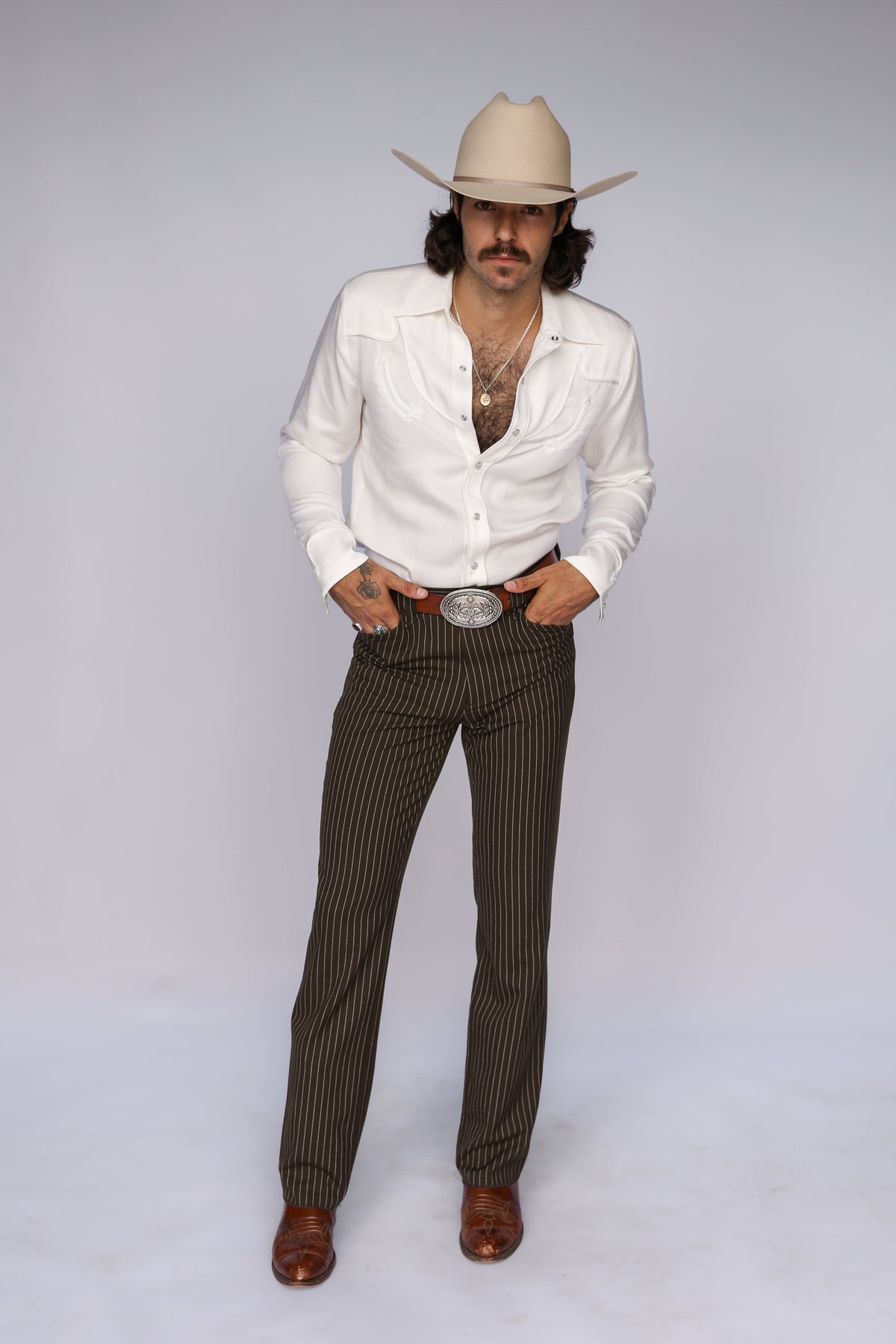 Man wearing the H Bar C Reno white western shirt open with a silver buckle and cream cowboy hat.
