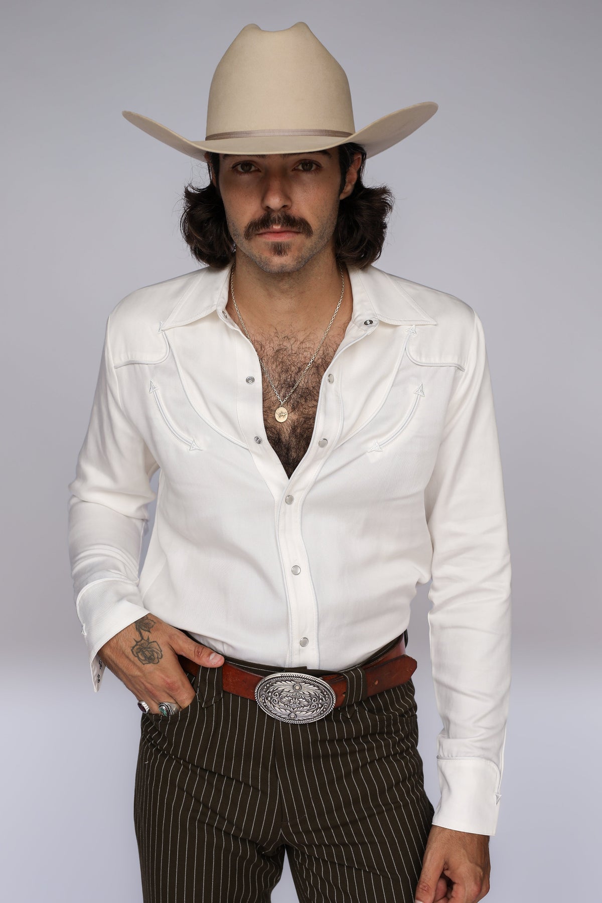Man in a cream cowboy hat wearing the H Bar C Reno men's shirt in white with whipstitch details, with brown pinstripe pants.