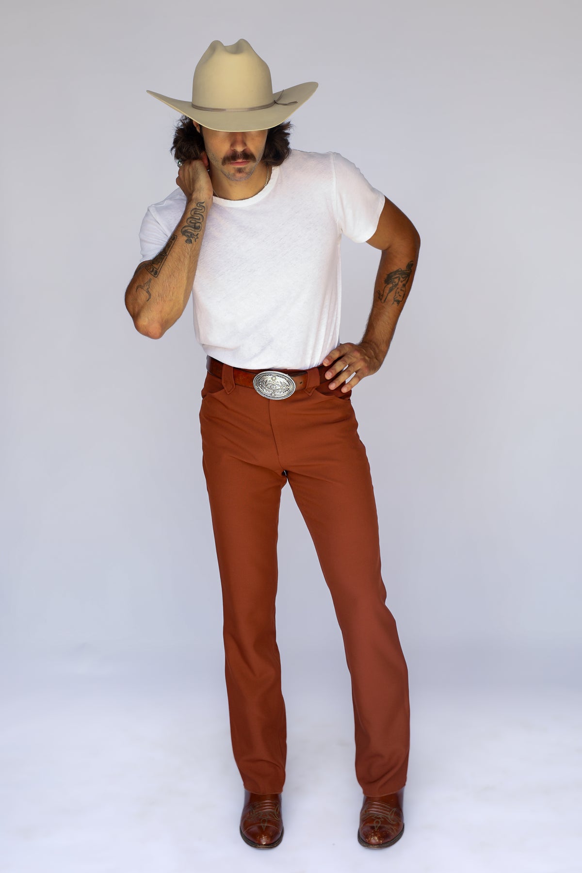 Man in a cowboy hat wearing the H Bar C Franklin unisex western pants in brown with a white tee and silver buckle.
