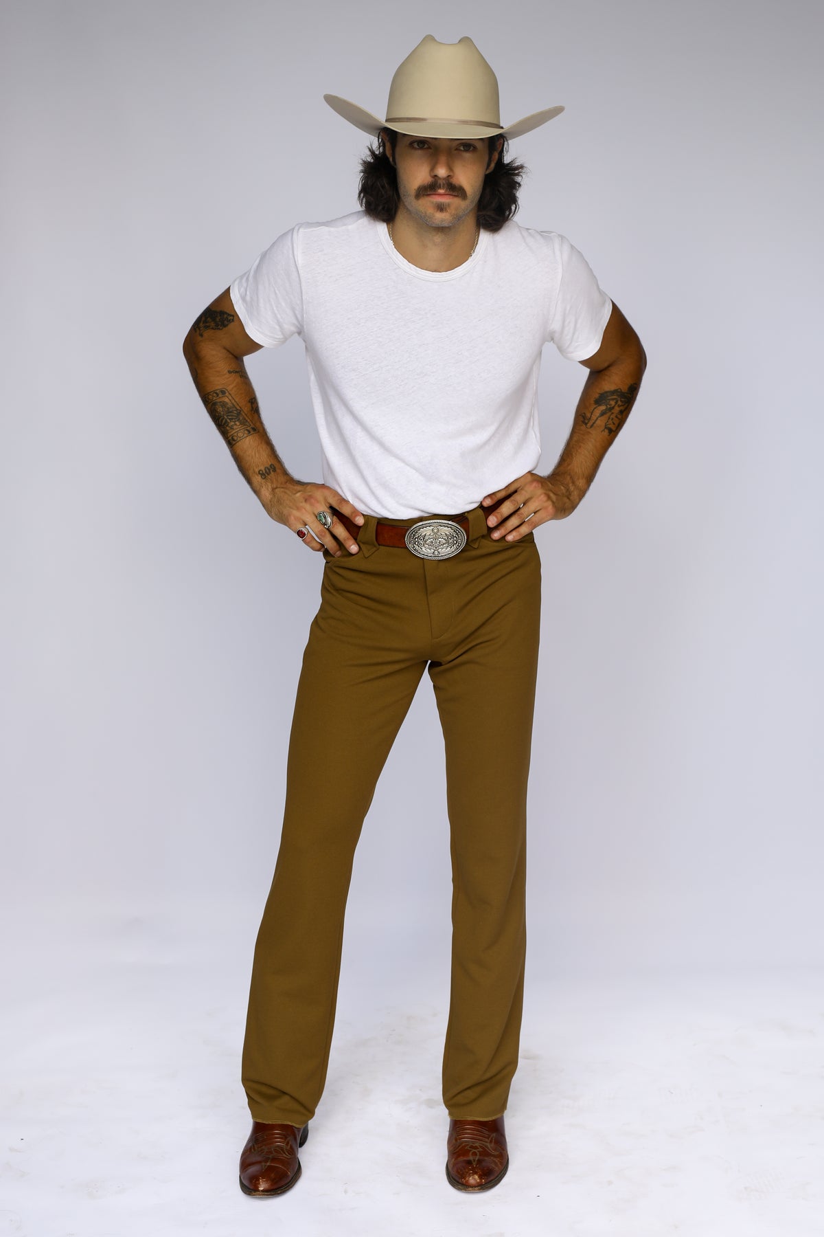 Man in a cowboy hat wearing the H Bar C Franklin olive green western pants with a white tee and silver buckle.