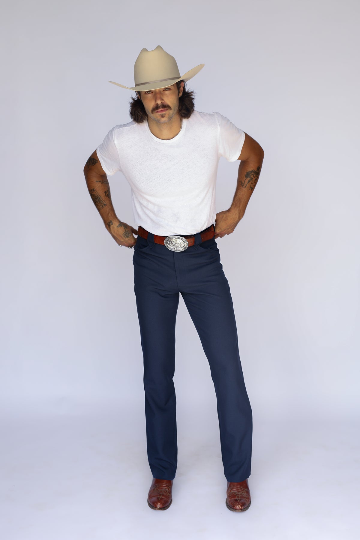 Front view of the H Bar C Franklin navy western pants styled with a white tee, buckle, and cowboy boots.