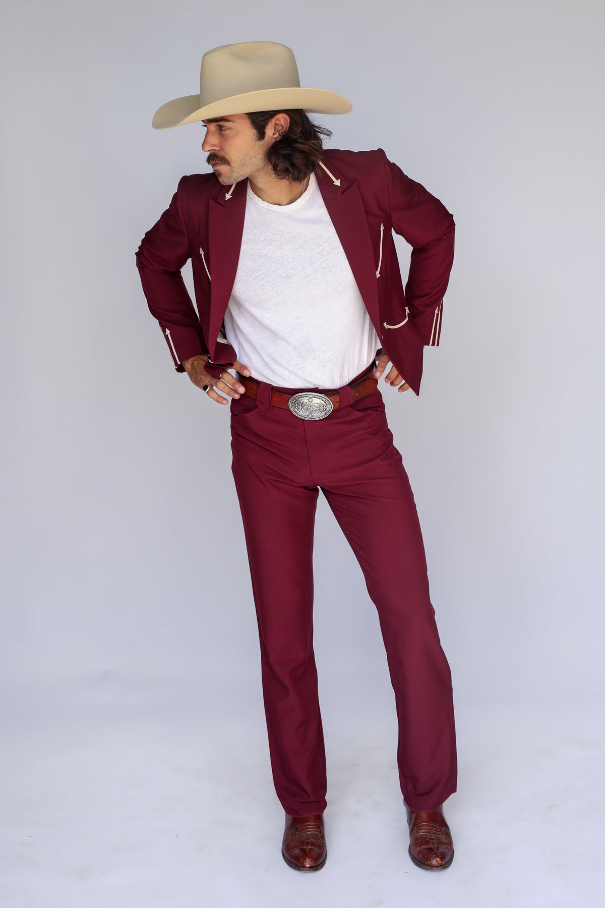 Man in a cowboy hat wearing the H Bar C Calamity maroon suit, jacket and matching western pants, hand on hip.
