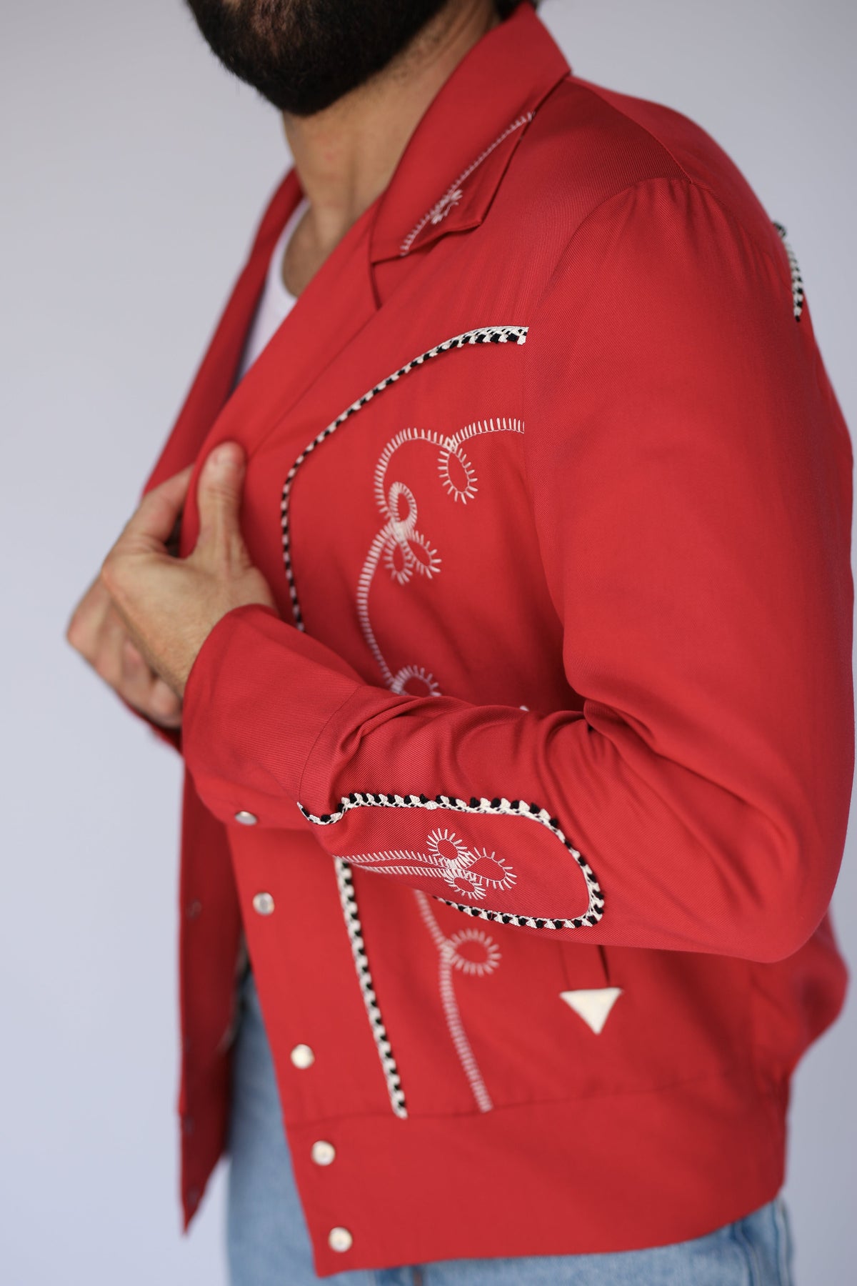 Side detail of the H Bar C Bolero red jacket sleeve with white embroidery and checkered piping.