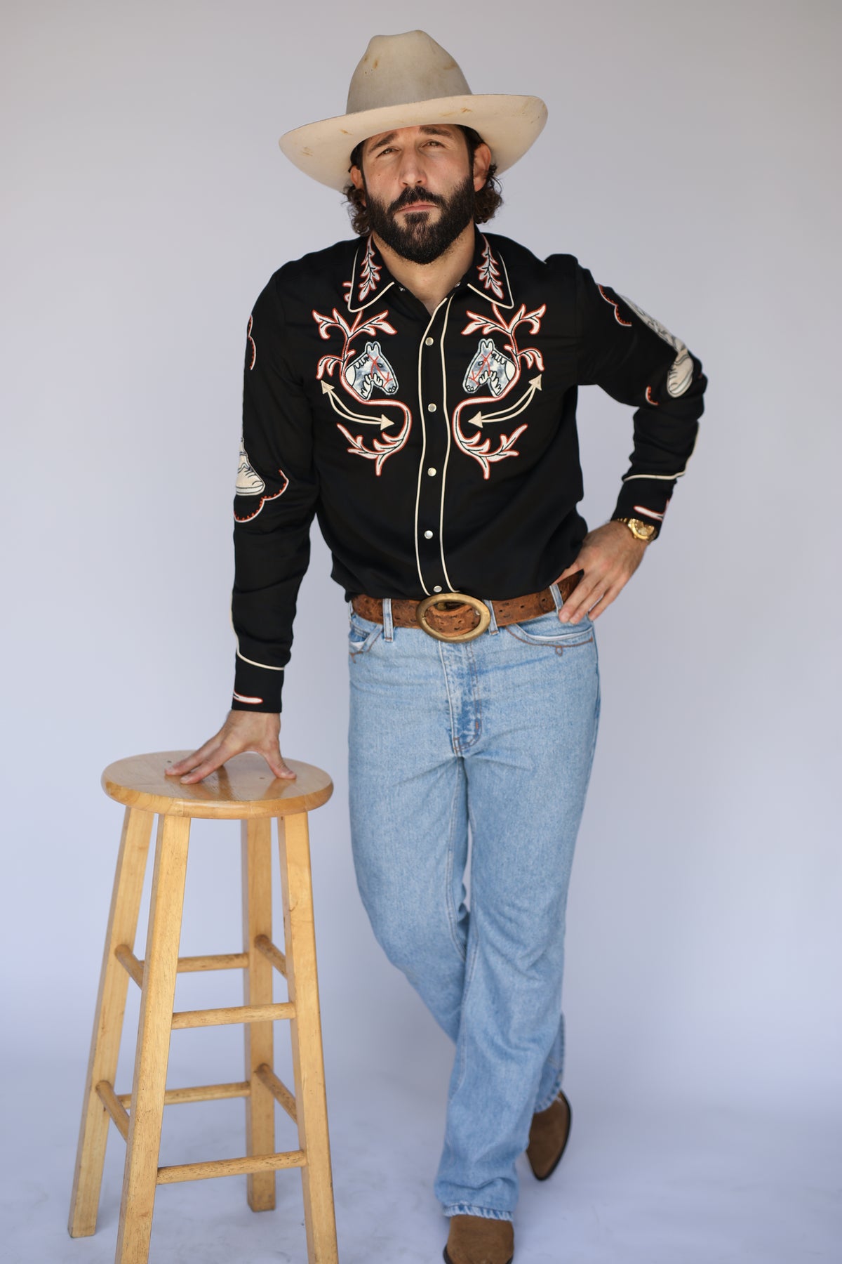 Man standing beside a stool in the H Bar C Calabasas black embroidered shirt and jeans.