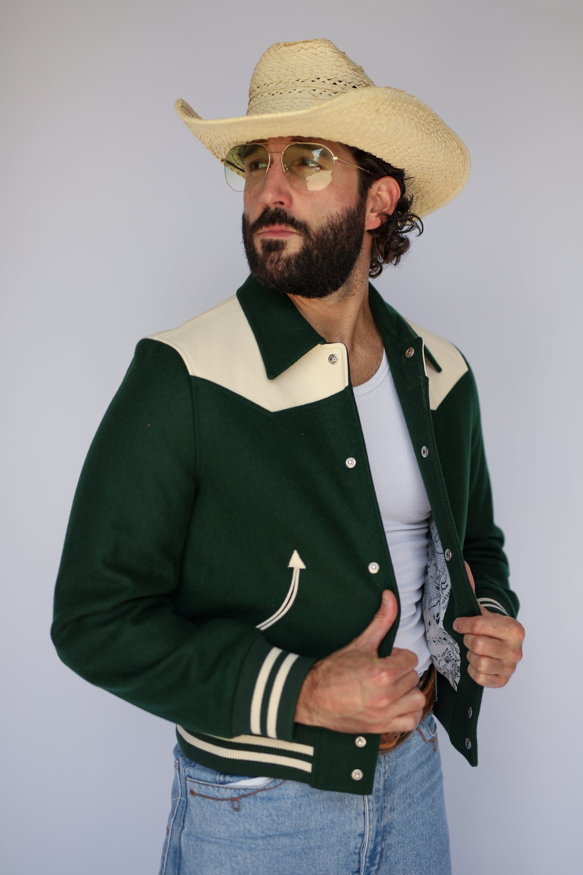 Front view of The Vail H Bar C green western varsity jacket worn open over a white tank.