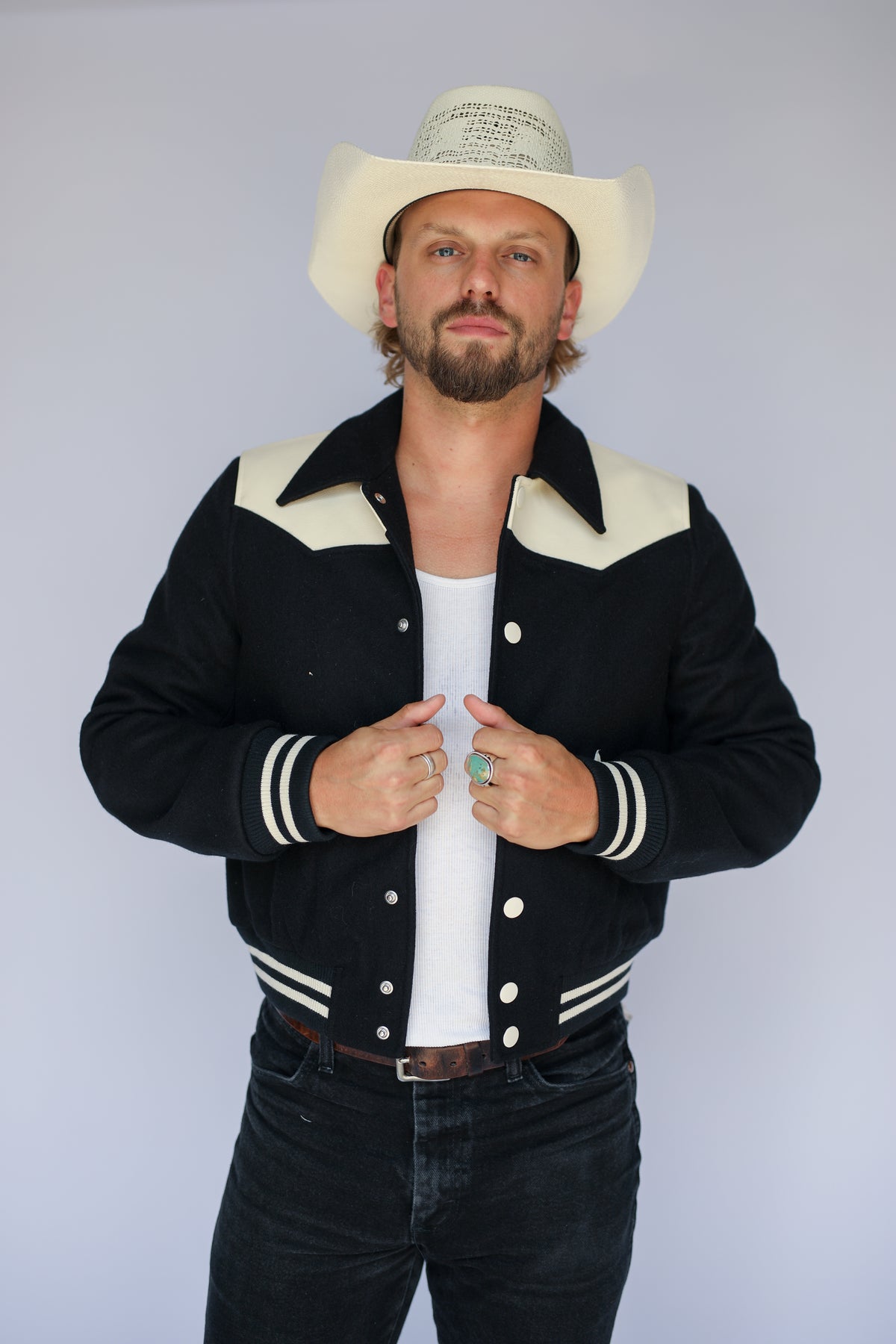 Front view of The Vail H Bar C black western varsity jacket with cream yoke over a white tank.