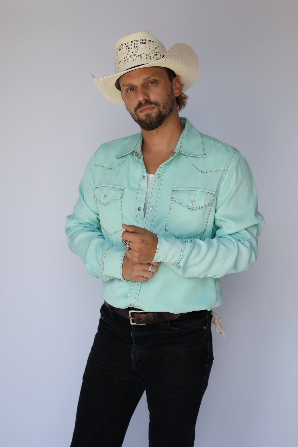 Man in a straw cowboy hat wearing the H Bar C Brooklyn men's shirt in turquoise with white contrast stitching, with black jeans.