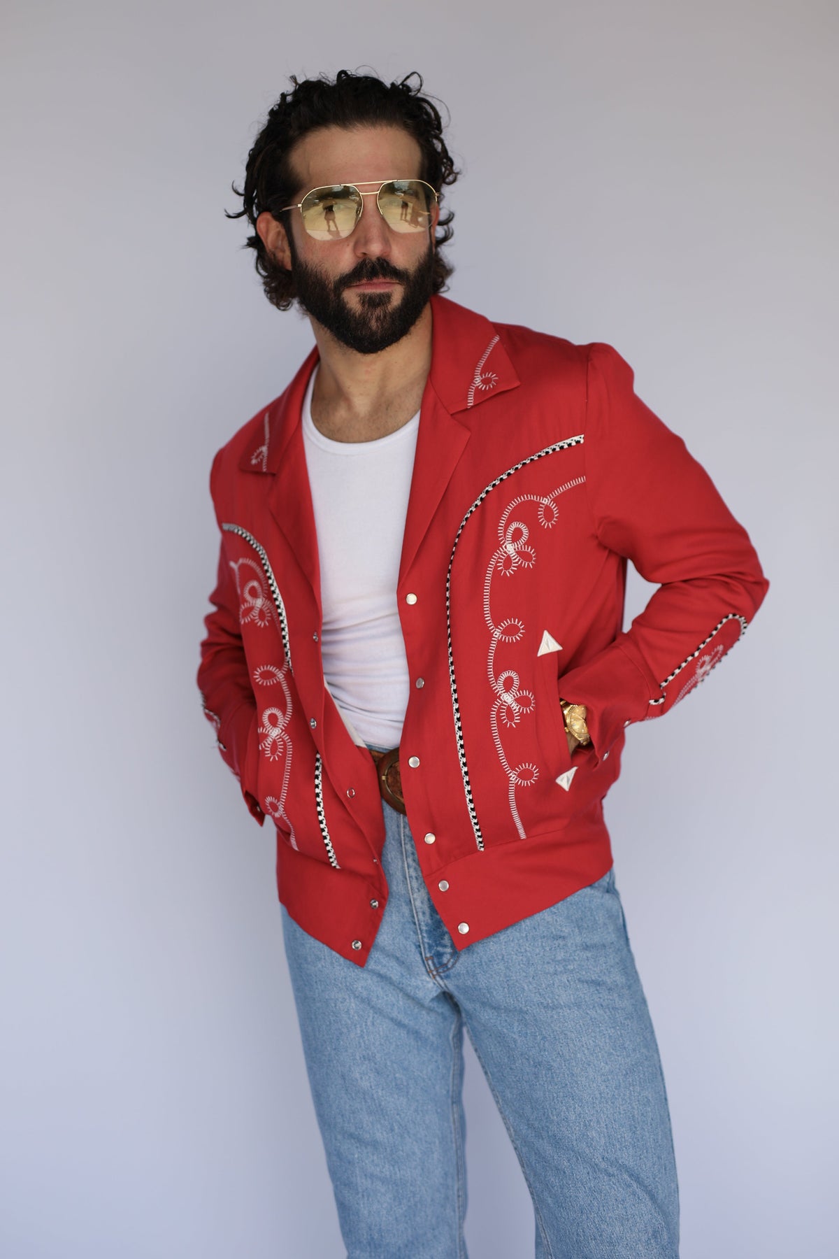 Man wearing the H Bar C Bolero men's jacket in red with white chain stitch embroidery, over a white tee with light jeans.