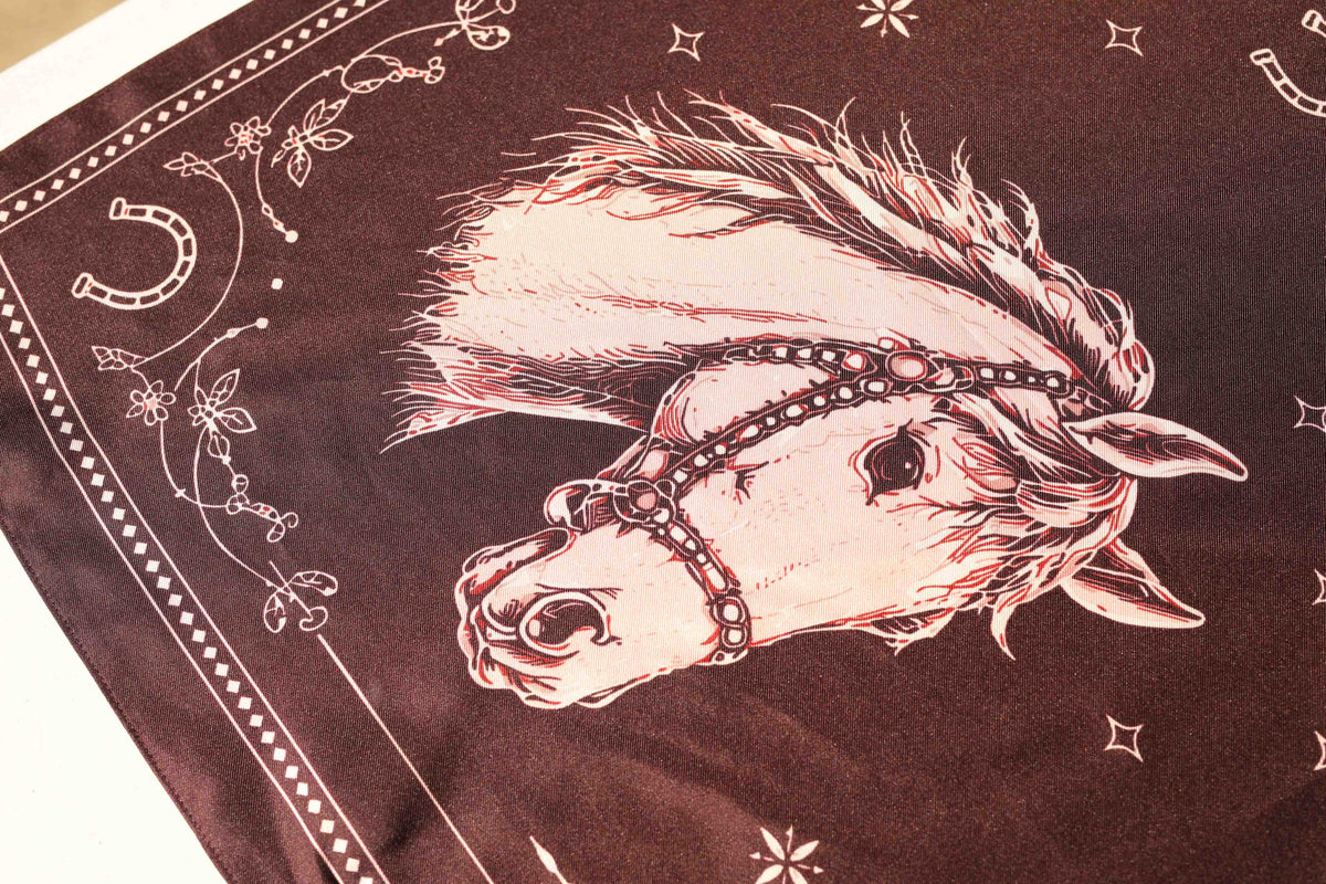 Close-up of the H Bar C Maroon Horse silk scarf showing a cream horse head with plumed mane and studded bridle beside a horseshoe on maroon silk.