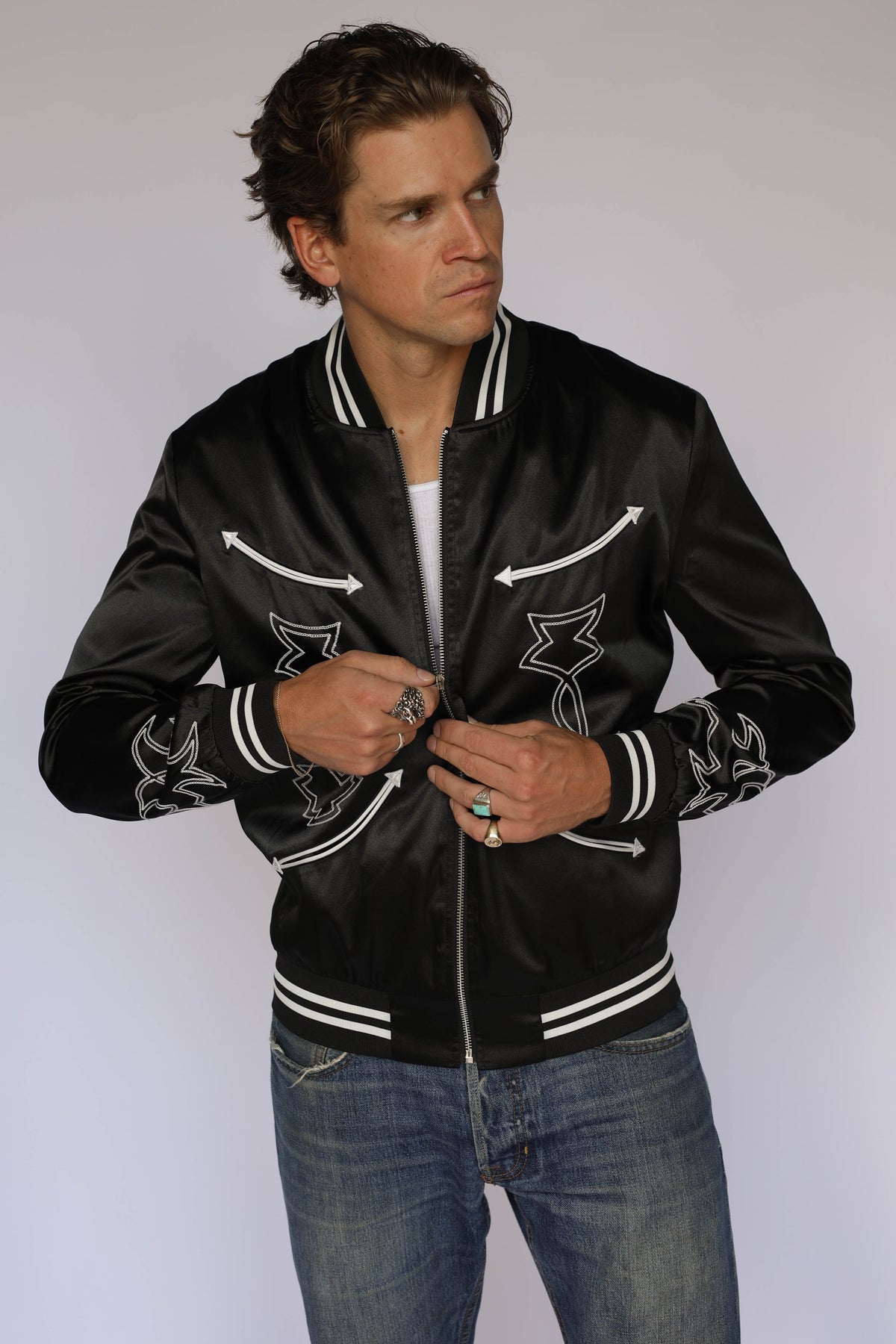 Man wearing the H Bar C Odessa Tour Jacket in black satin, vintage inspired western wear with white arrow appliqués and boot stitch embroidery.