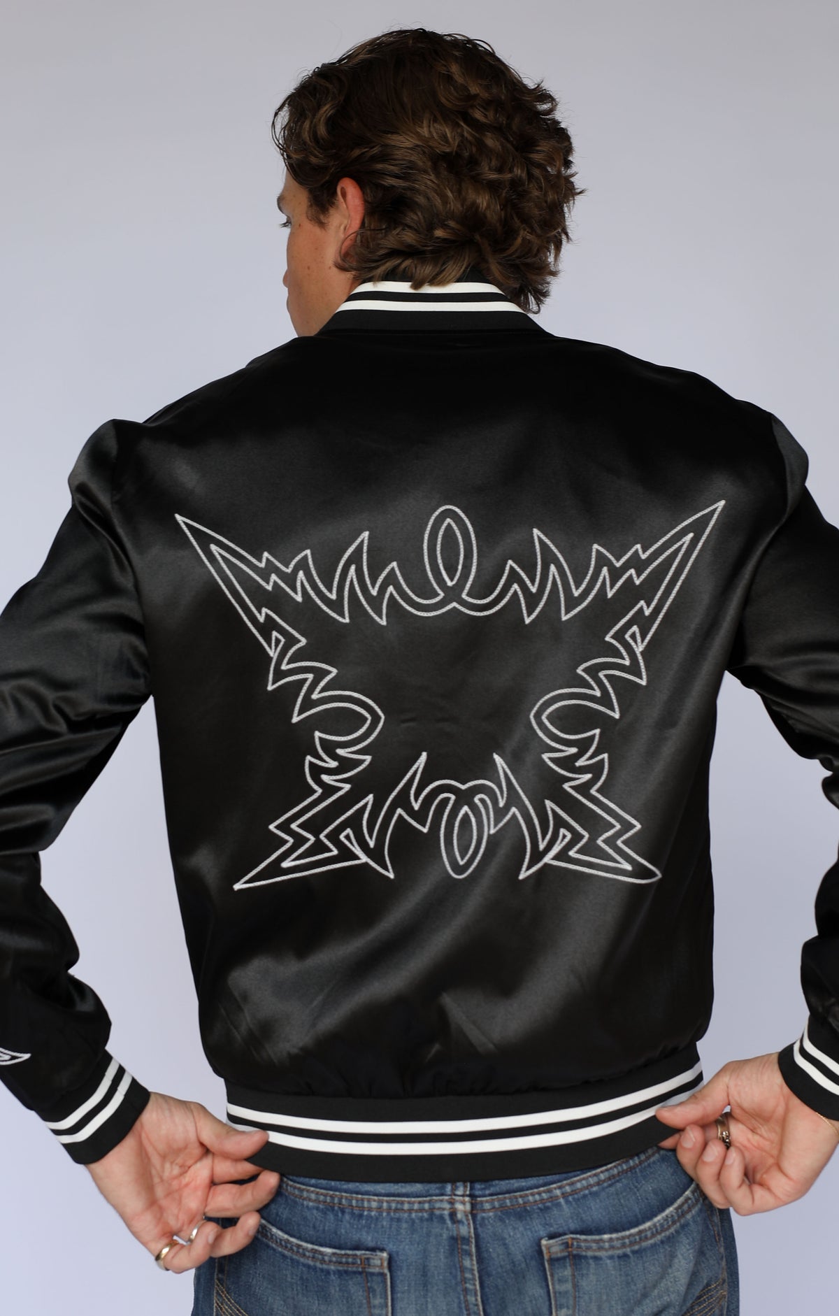 Back view of the H Bar C Odessa black satin tour jacket, vintage western wear with white chain stitch embroidery across the back.