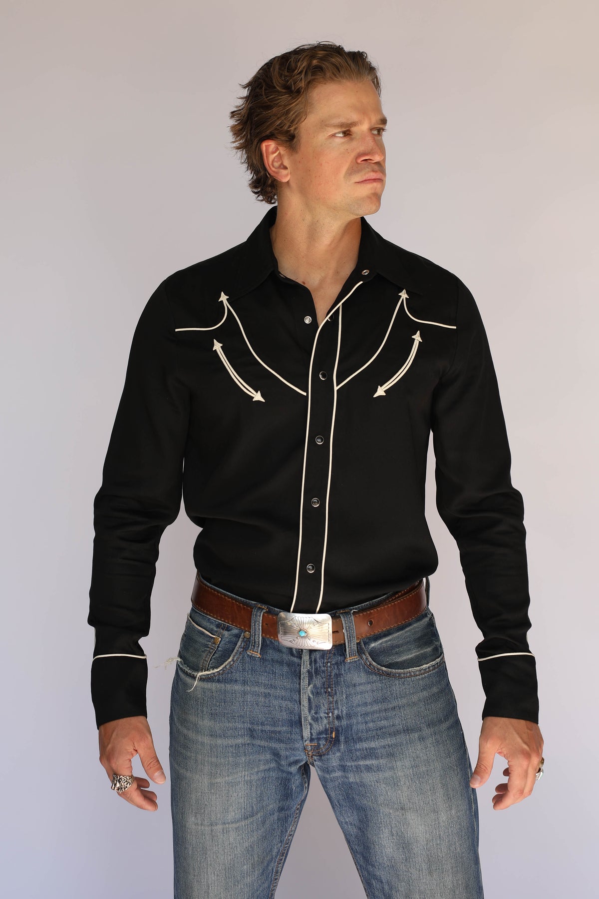 Model in the H Bar C Reno black western shirt tucked into jeans with a silver buckle, classic vintage western wear with contrast piping.