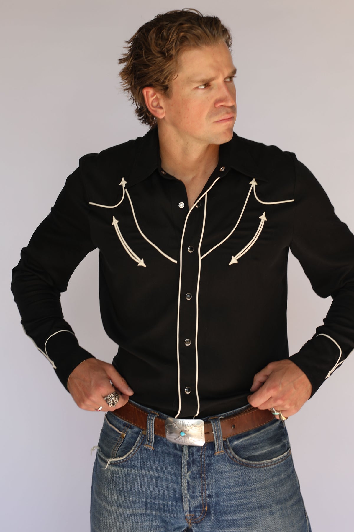 Man adjusting his cuff in the H Bar C Reno black western shirt, vintage western wear with off-white piped yokes and arrow details.