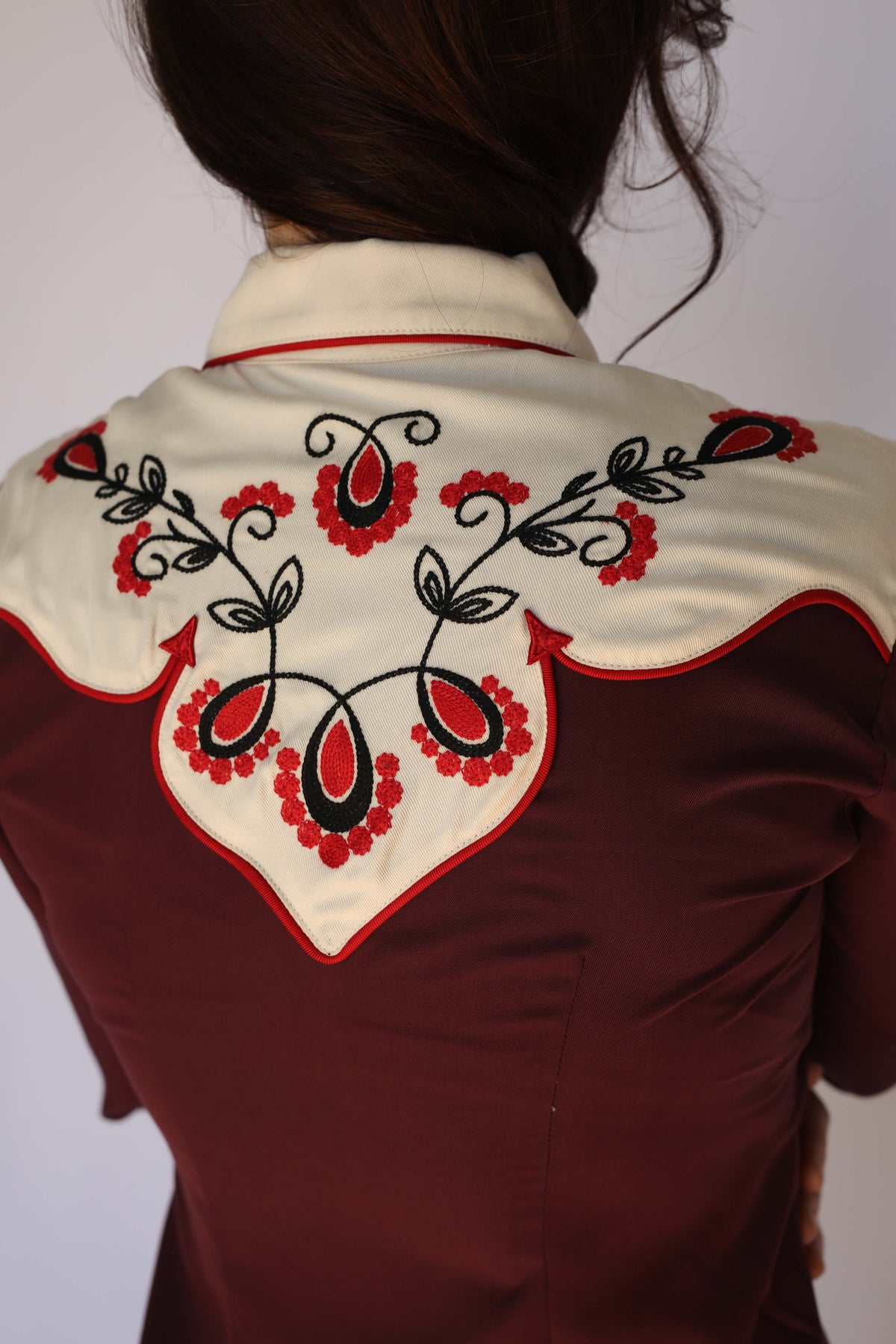 Close-up of the cream back yoke on the H Bar C San Jose women's burgundy shirt with red and black chain stitch floral embroidery, red piping, and arrow tips, vintage western wear.