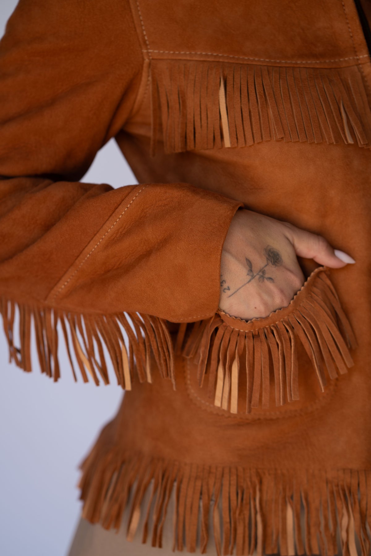 Close-up of the H Bar C Omaha rust brown suede fringe jacket with hand in the front pocket.