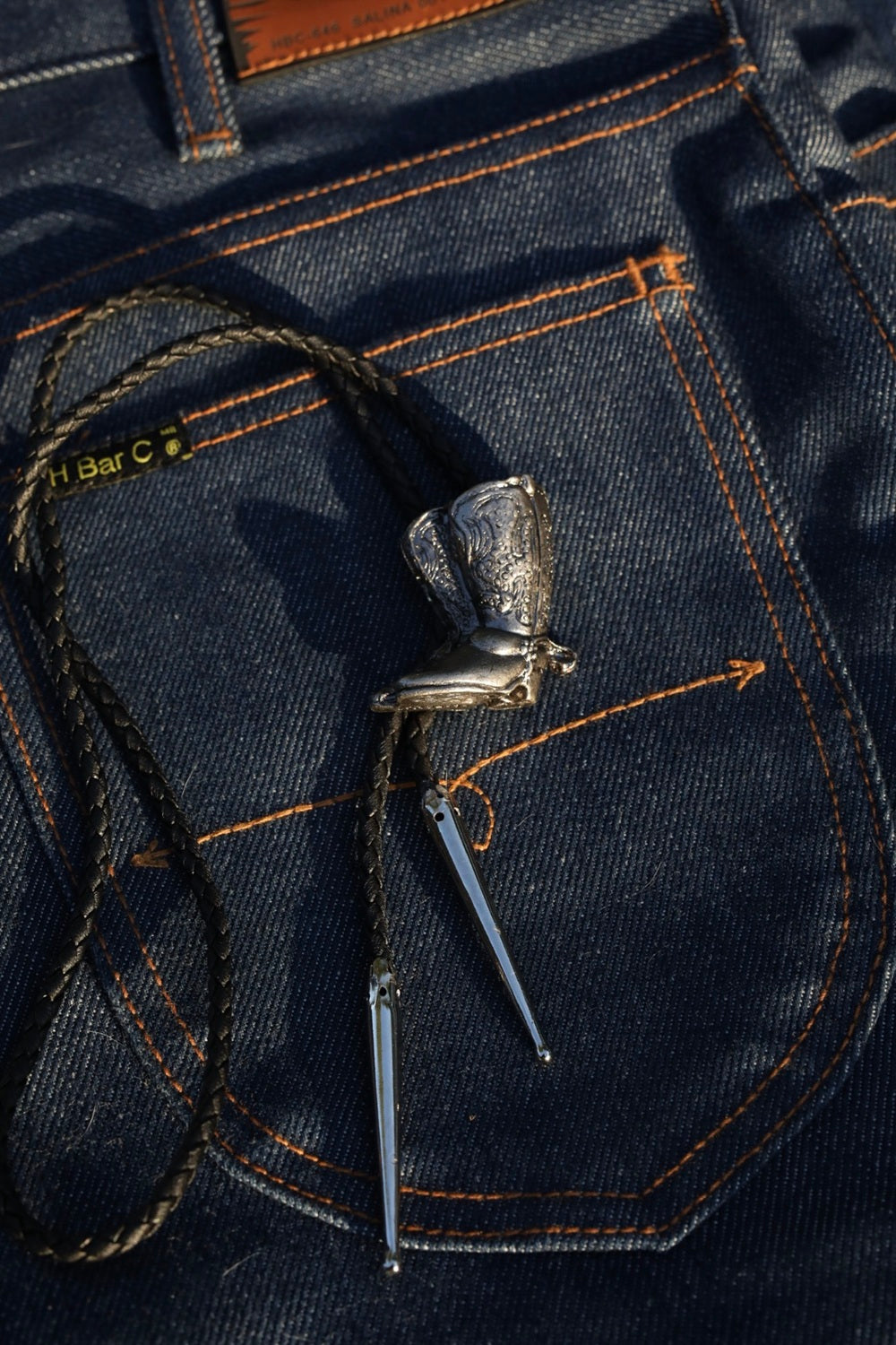 H Bar C heritage bolo tie with cowboy boot slide on raw denim.