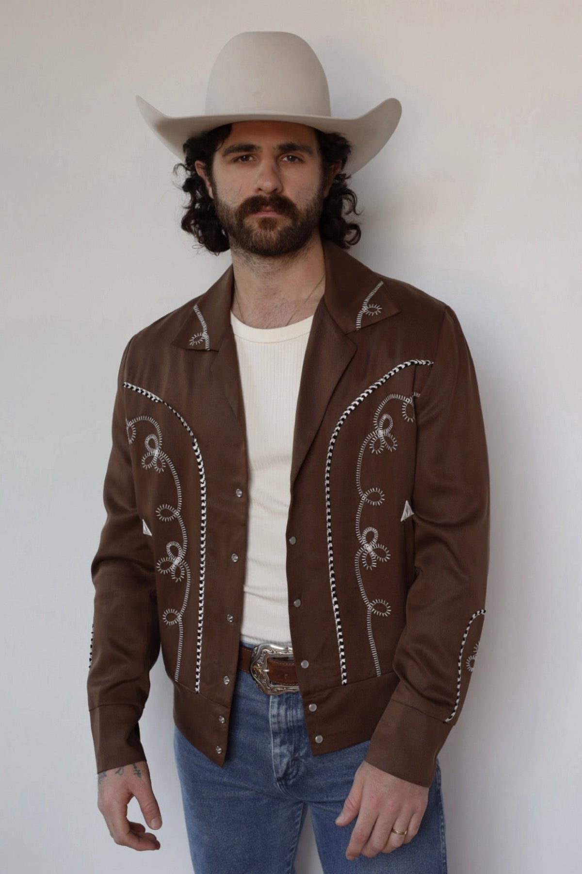 Man in a white cowboy hat wearing the H Bar C Bolero men's jacket in walnut brown with white embroidery, designed for Bob Wills in 1936.