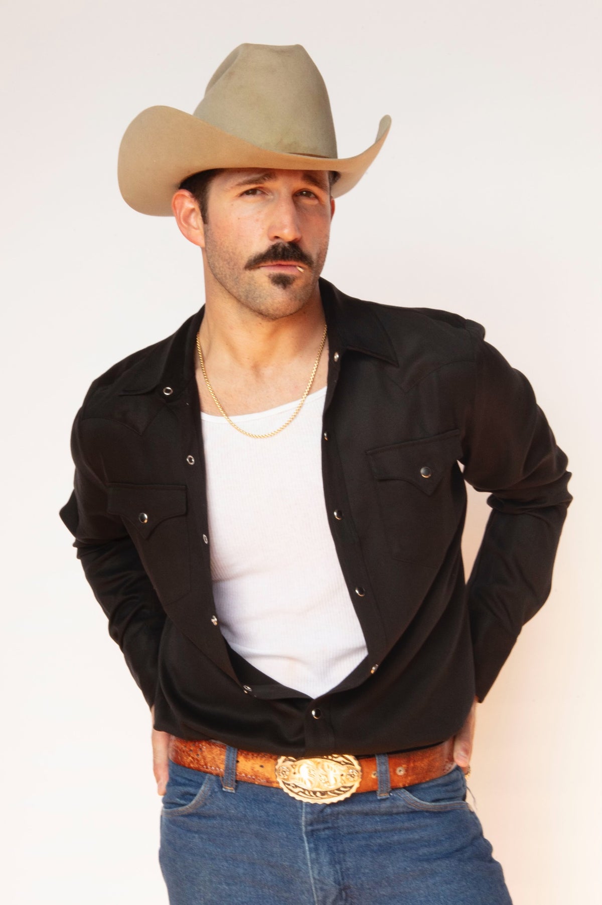 Man in a cowboy hat wearing the H Bar C Denver men's shirt in black open over a white tank with jeans and a western buckle.