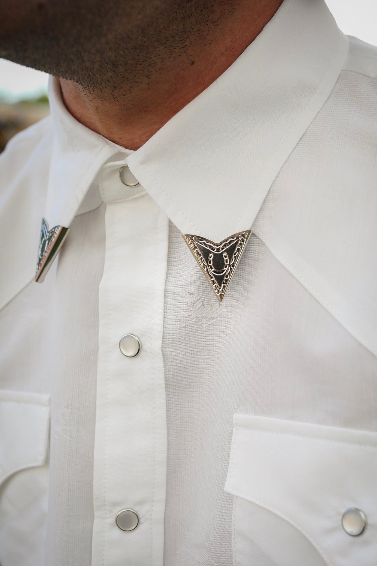Engraved silver western collar tips by H Bar C worn on a white pearl snap shirt, from Five Pieces of the Frontier.