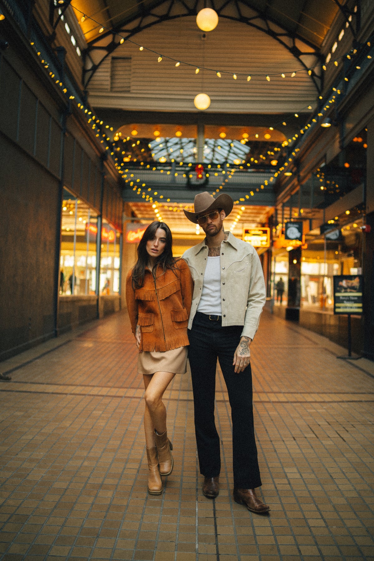 Couple walking through a lit arcade, the woman wearing the H Bar C Omaha suede fringe jacket.