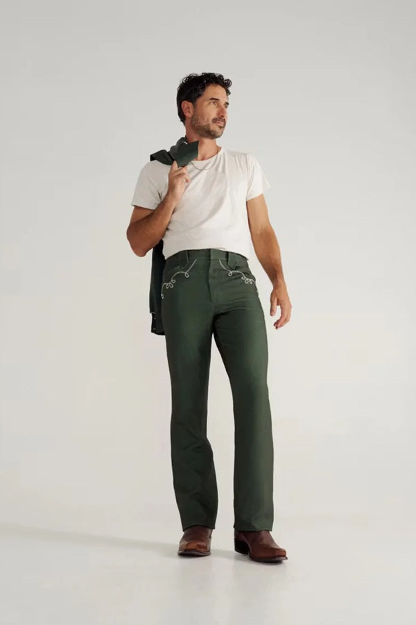 Man wearing the Tecovas x H Bar C Birthday X pant in Tecovas green with a white tee, holding the matching jacket.
