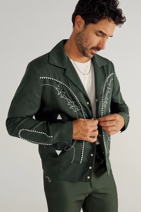 Man wearing the Tecovas x H Bar C Birthday X Bolero jacket in green with white chain stitch and arrowheads, a 10th anniversary collaboration.