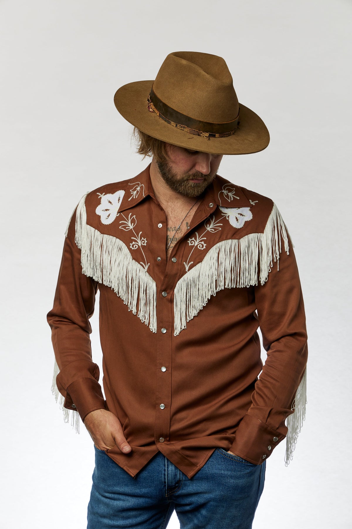 Front view of the H Bar C Taos brown and white fringe shirt with a felt cowboy hat.