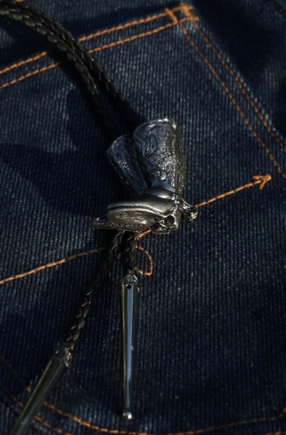 Close-up of the H Bar C cowboy boots bolo tie slide and silver tips on denim.