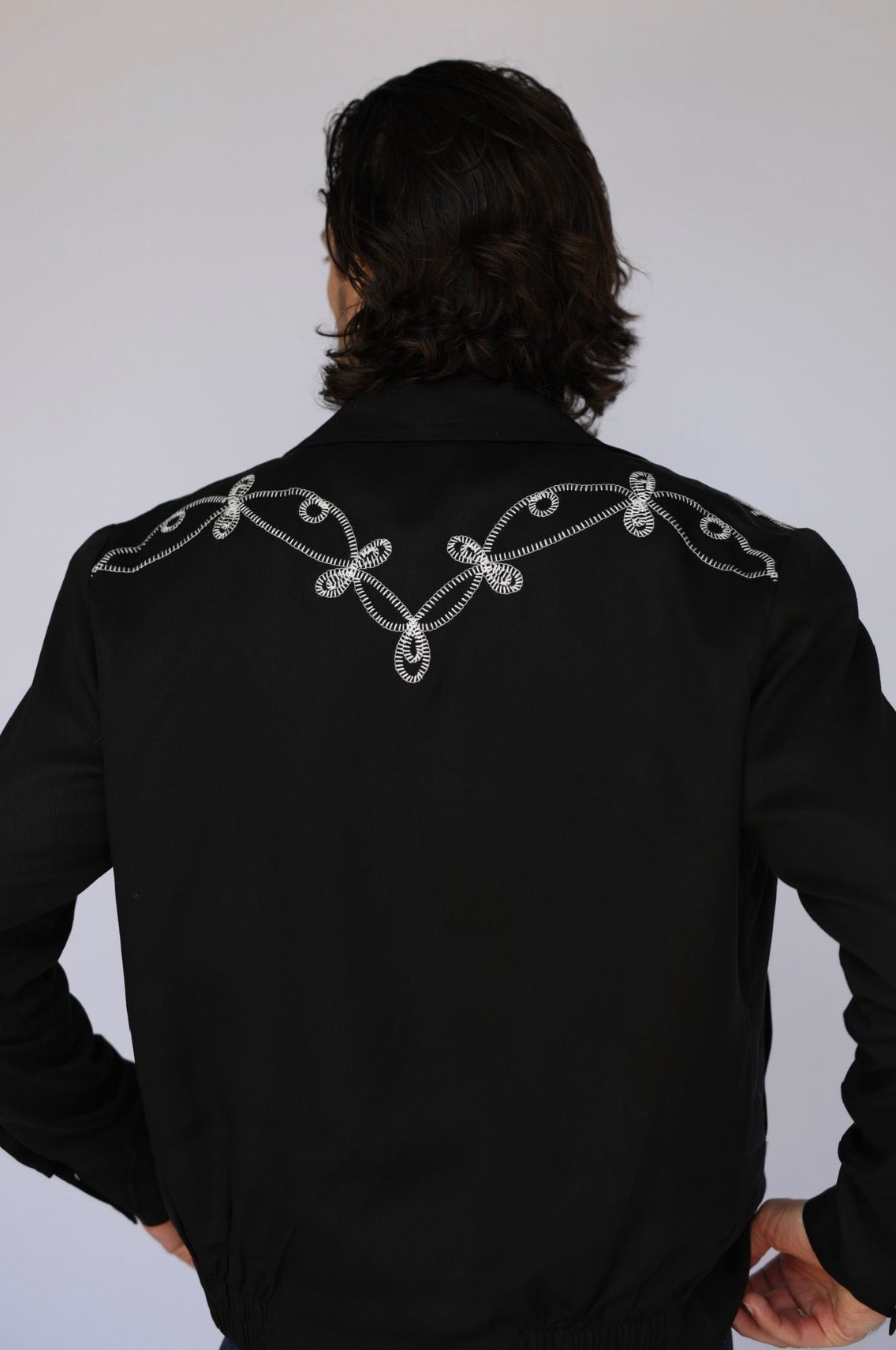 Back view of the H Bar C Bolero El Patrón black jacket with white scrollwork embroidery across the shoulders.