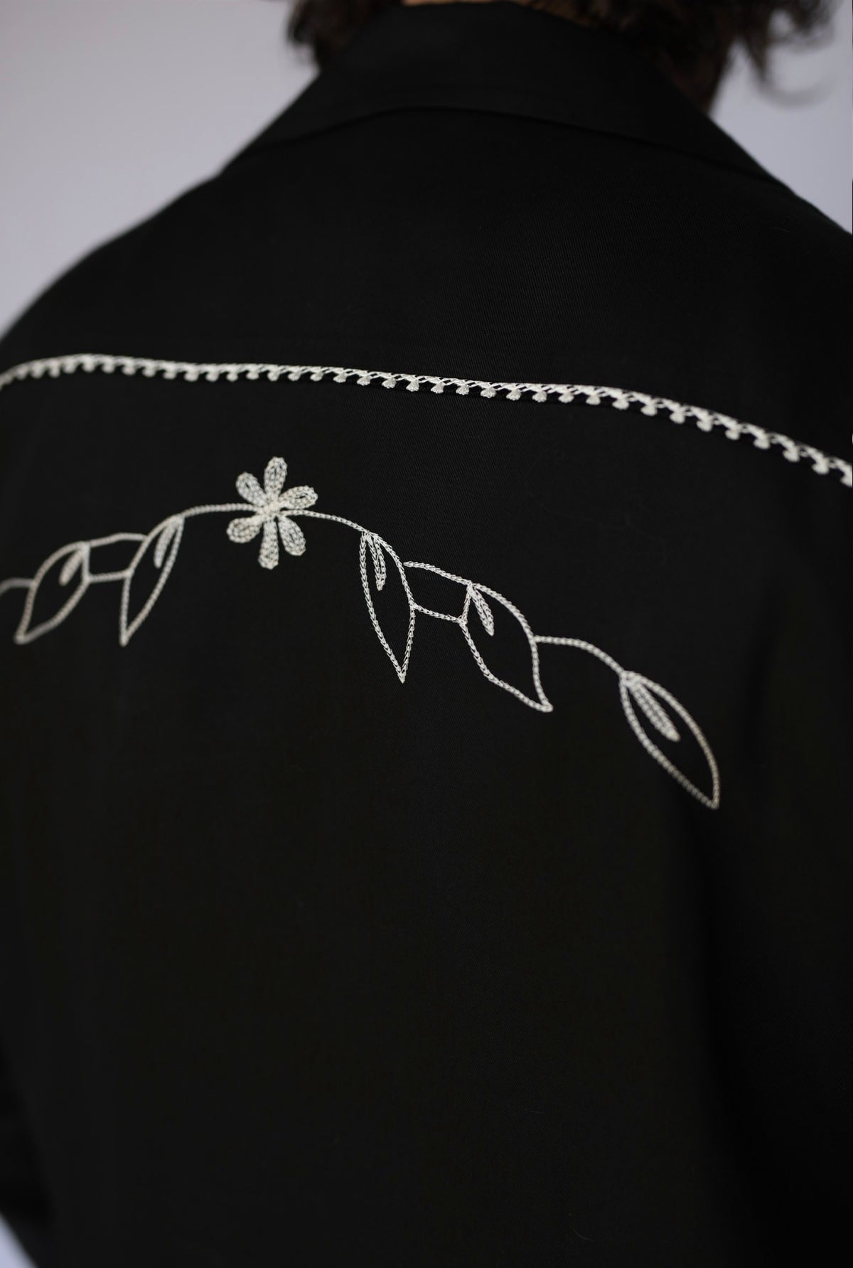Back yoke detail of the H Bar C Bolero Nogales black jacket with white floral chain stitch embroidery.