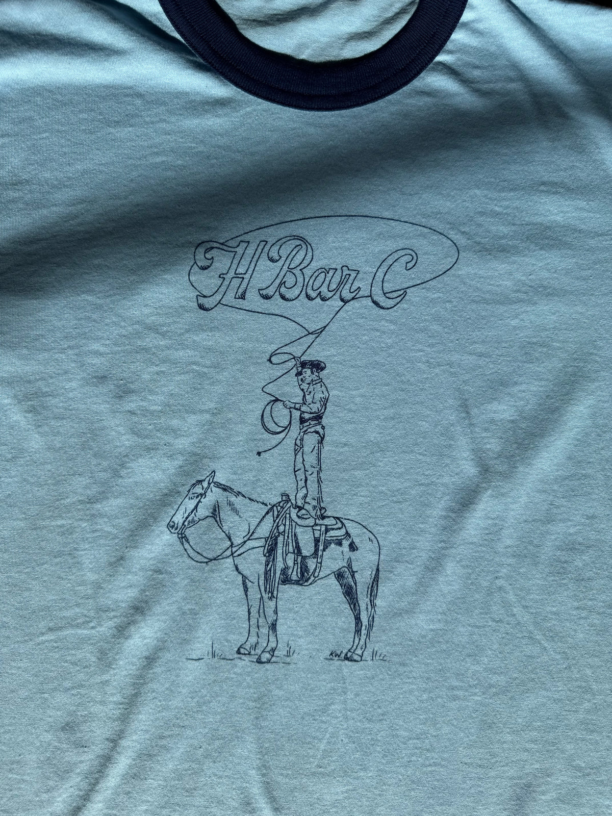 Close-up of the Kate Snake Art cowboy standing on horse and H Bar C lasso logo on the blue ringer tee.
