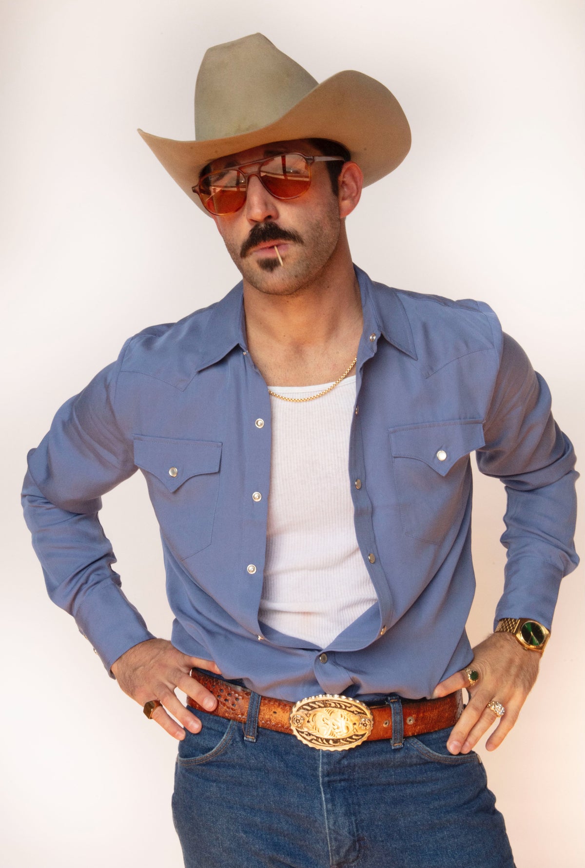 Man with hands on hips wearing the H Bar C Denver periwinkle pearl snap shirt open over a white tank.